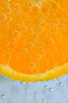 Slice of ripe orange fruit in water on white background. Close-up of orange fruit in liquid with bubbles. Slice of ripe orange fruit in sparkling water. Macro image of fruit in carbonated water