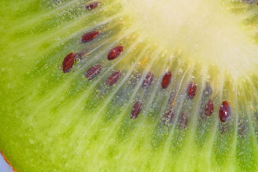 Close-up of a kiwi fruit slice in liquid with bubbles. Slice of ripe kiwi fruit in water. Close-up of fresh kiwi slice covered by bubbles. Macro horizontal image