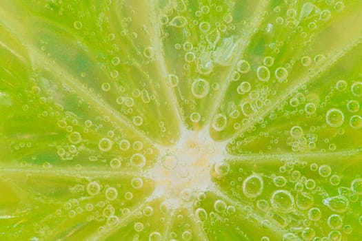 Slice of ripe lime in water. Close-up of lime in liquid with bubbles. Slice of ripe lime in sparkling water. Macro horizontal image of fruit in carbonated water