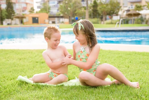 Theme is a children's summer vacation. Two Caucasian children, brother and sister, sit in a perched round pool with water in the yard of the green grass in a bathing suit and joy happiness smile.