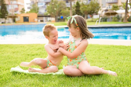 Theme is a children's summer vacation. Two Caucasian children, brother and sister, sit in a perched round pool with water in the yard of the green grass in a bathing suit and joy happiness smile.