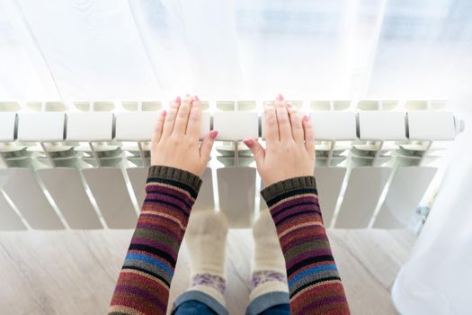 Girl warms up the frozen hands above hot radiator, close up