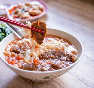Beef noodle - Taiwan ramen meal with tomato sauce broth in bowl on bright wooden table, famous chinese style food, close up, top view, copy space