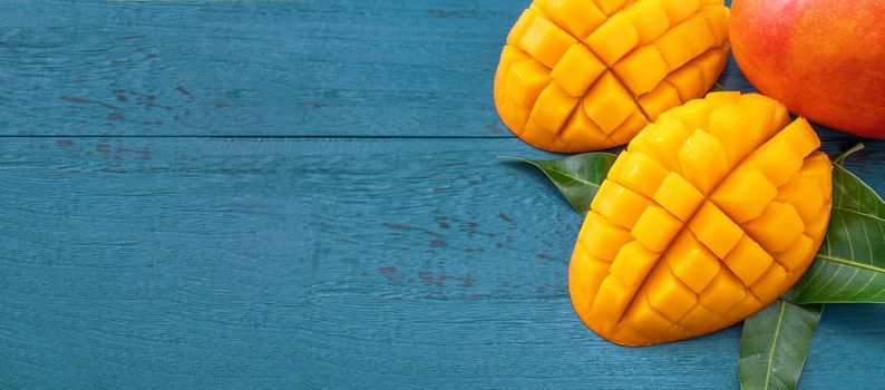 Fresh mango - beautiful chopped fruit with green leaves on dark blue timber background. Tropical fruit design concept. Flat lay. Top view. Copy space