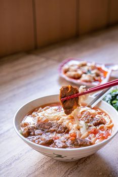 Beef noodle - Taiwan ramen meal with tomato sauce broth in bowl on bright wooden table, famous chinese style food, close up, top view, copy space