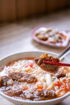 Beef noodle - Taiwan ramen meal with tomato sauce broth in bowl on bright wooden table, famous chinese style food, close up, top view, copy space