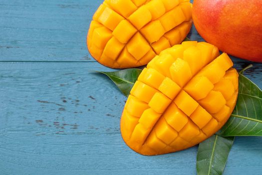 Fresh mango - beautiful chopped fruit with green leaves on dark blue timber background. Tropical fruit design concept. Flat lay. Top view. Copy space