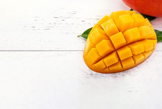 Beautiful chopped mango chunks with green leaves on bright white color timber background. Copy space, close up, macro. Tropical fruit concept.