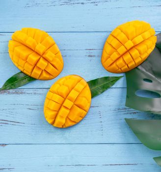 Fresh mango - beautiful chopped fruit with green leaves on bright blue timber background. Tropical fruit design concept. Flat lay. Top view. Copy space