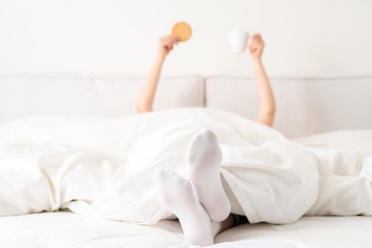 Female hand holding cup of coffee from under a blanket in bed. Woman waking up in the morning.