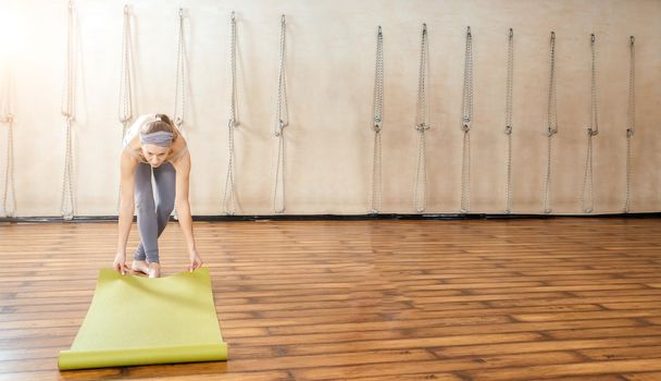 Young woman rolling yoga mat in yoga studio before training class