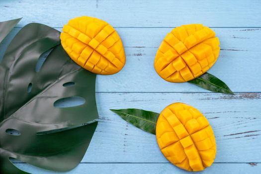 Fresh mango - beautiful chopped fruit with green leaves on bright blue timber background. Tropical fruit design concept. Flat lay. Top view. Copy space