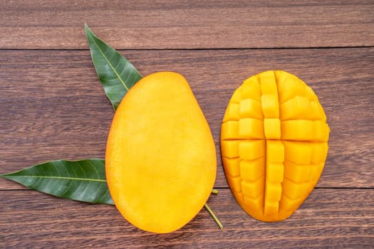 Fresh mango - beautiful chopped fruit with green leaves on dark wood background. Tropical fruit design concept. Flat lay. Top view. Copy space.