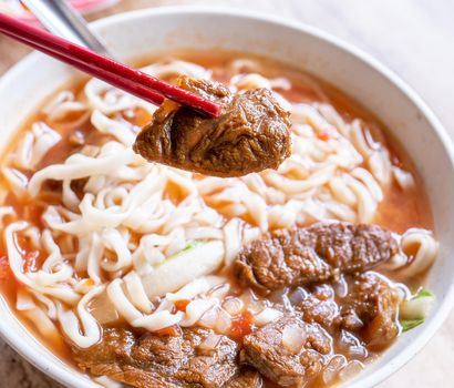 Beef noodle - Taiwan ramen meal with tomato sauce broth in bowl on bright wooden table, famous chinese style food, close up, top view, copy space