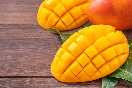 Fresh mango - beautiful chopped fruit with green leaves on dark wood background. Tropical fruit design concept. Flat lay. Top view. Copy space.