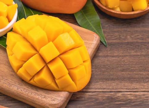 Fresh chopped mango cubes on wooden cutting board and rustic timber background. Tropical summer fruit concept, close up, macro, copy space.