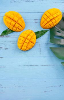 Fresh mango - beautiful chopped fruit with green leaves on bright blue timber background. Tropical fruit design concept. Flat lay. Top view. Copy space