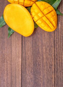 Fresh mango - beautiful chopped fruit with green leaves on dark wooden timber background. Tropical fruit design concept. Flat lay. Top view. Copy space
