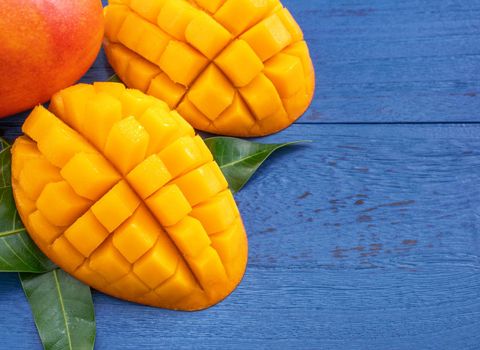 Fresh mango - beautiful chopped fruit with green leaves on dark blue timber background. Tropical fruit design concept. Flat lay. Top view. Copy space