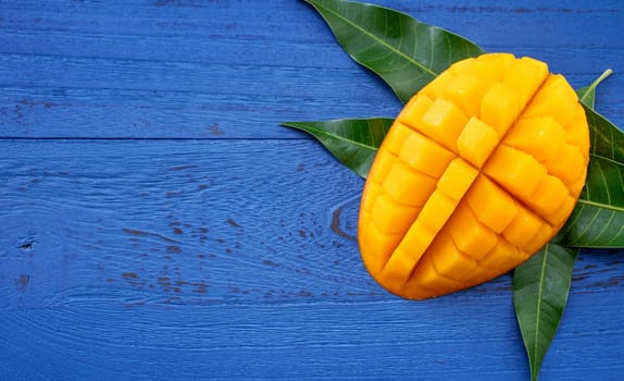 Fresh mango - beautiful chopped fruit with green leaves on dark blue timber background. Tropical fruit design concept. Flat lay. Top view. Copy space