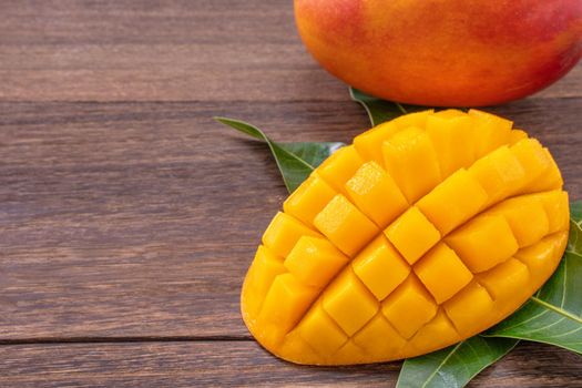Fresh mango - beautiful chopped fruit with green leaves on dark wooden timber background. Tropical fruit design concept. Flat lay. Top view. Copy space
