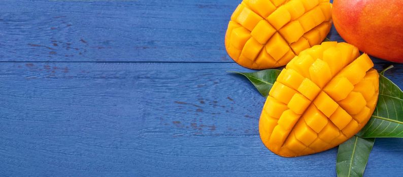 Fresh mango - beautiful chopped fruit with green leaves on dark blue timber background. Tropical fruit design concept. Flat lay. Top view. Copy space