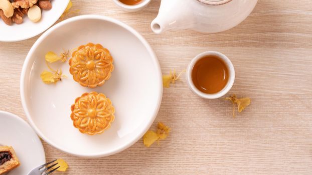 Delicious moon cake for Mid-Autumn festival with beautiful pattern, decorated with yellow flowers and tea. Concept of festive afternoon pastry design