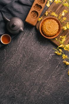 Mid-Autumn Festival traditional food concept - Beautiful Moon cake on black slate table with tea, pastry mold, flower, top view, flat lay, copy space