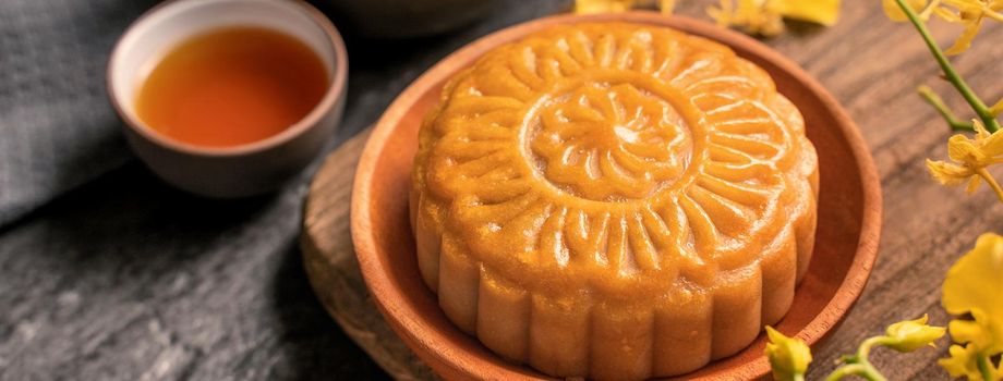 Mid-Autumn Festival traditional food concept - Beautiful Moon cake on black slate table with tea, pastry mold, flower, close up, copy space