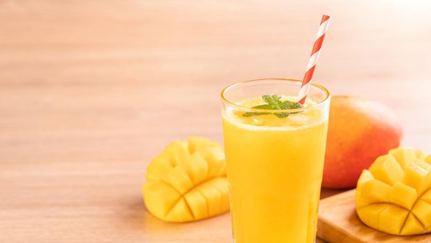 Fresh mango juice with beautiful chopped pulp flesh on bright wooden table background. Tropical fruit drink design concept. Close up, copy space.