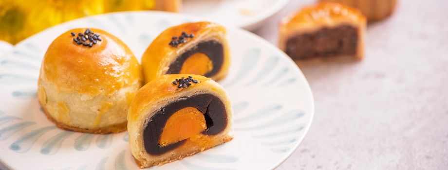 Mid-Autumn Festival traditional food concept - Beautiful cut moon cake on blue pattern plate on white background with flower, close up, copy space