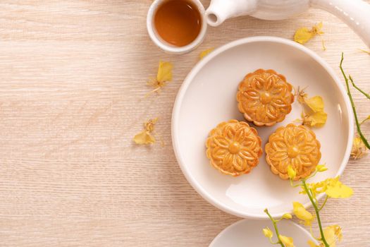 Tasty moon cake for Mid-Autumn festival on bright wooden table, concept of festive afternoon tea decorated with yellow flowers, top view, flat lay.
