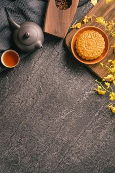 Mid-Autumn Festival traditional food concept - Beautiful Moon cake on black slate table with tea, pastry mold, flower, top view, flat lay, copy space