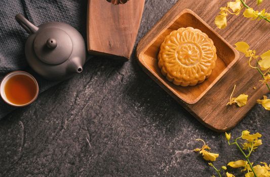 Mid-Autumn Festival traditional food concept - Beautiful Moon cake on black slate table with tea, pastry mold, flower, top view, flat lay, copy space