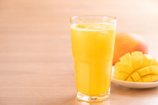 Fresh mango juice with beautiful chopped pulp flesh and straw on bright wooden table background. Tropical fruit design concept. Close up, copy space.
