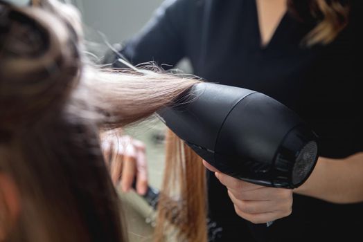 Close up of hairdressers hands drying long blond hair with blow dryer
