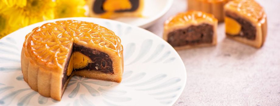 Mid-Autumn Festival traditional food concept - Beautiful cut moon cake on blue pattern plate on white background with flower, close up, copy space