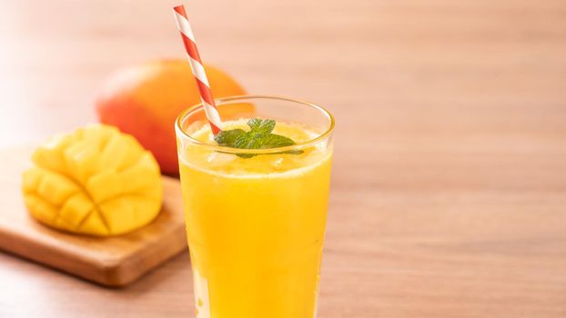 Fresh mango juice with beautiful chopped pulp flesh on bright wooden table background. Tropical fruit drink design concept. Close up, copy space.