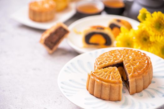 Mid-Autumn Festival traditional food concept - Beautiful cut moon cake on blue pattern plate on white background with flower, close up, copy space