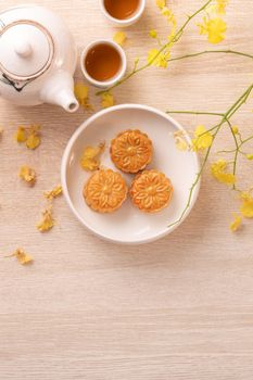 Tasty moon cake for Mid-Autumn festival on bright wooden table, concept of festive afternoon tea decorated with yellow flowers, top view, flat lay.