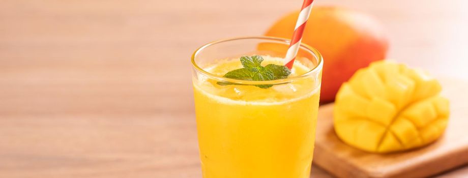 Fresh mango juice with beautiful chopped pulp flesh on bright wooden table background. Tropical fruit drink design concept. Close up, copy space.