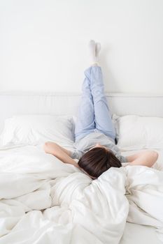 Female legs raised up high and arms under her head lying on bed in bedroom