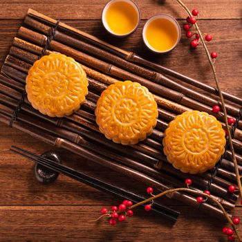 Chinese traditional pastry Moon cake Mooncake with tea cups on bamboo serving tray on wooden background for Mid-Autumn Festival, top view, flat lay.