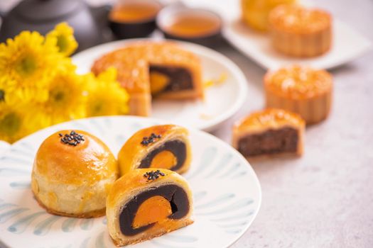 Mid-Autumn Festival traditional food concept - Beautiful cut moon cake on blue pattern plate on white background with flower, close up, copy space