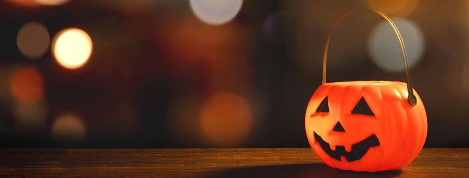 Halloween concept - Orange plastic pumpkin lantern on a dark wooden table with blurry sparkling light in the background, trick or treat, close up.