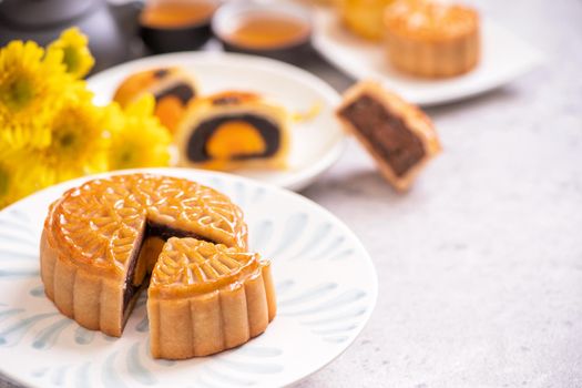 Mid-Autumn Festival traditional food concept - Beautiful cut moon cake on blue pattern plate on white background with flower, close up, copy space
