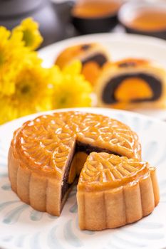 Mid-Autumn Festival traditional food concept - Beautiful cut moon cake on blue pattern plate on white background with flower, close up, copy space