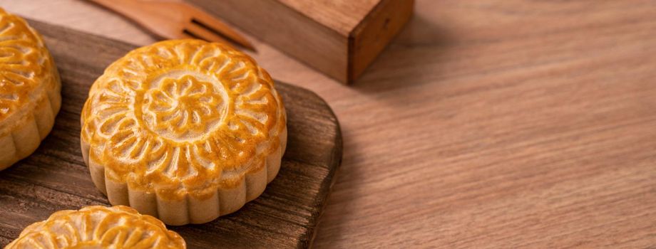 Round shaped fresh baked moon cake pastry - Chinese moonckae for Mid-Autumn Moon Festival on wooden background and serving tray, close up, copy space