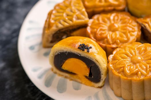 Tasty baked egg yolk pastry moon cake for Mid-Autumn Festival on black slate dark background. Chinese festive food concept, close up, copy space.