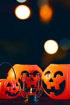 Halloween concept - Orange plastic pumpkin lantern on a dark wooden table with blurry sparkling light in the background, trick or treat, close up.